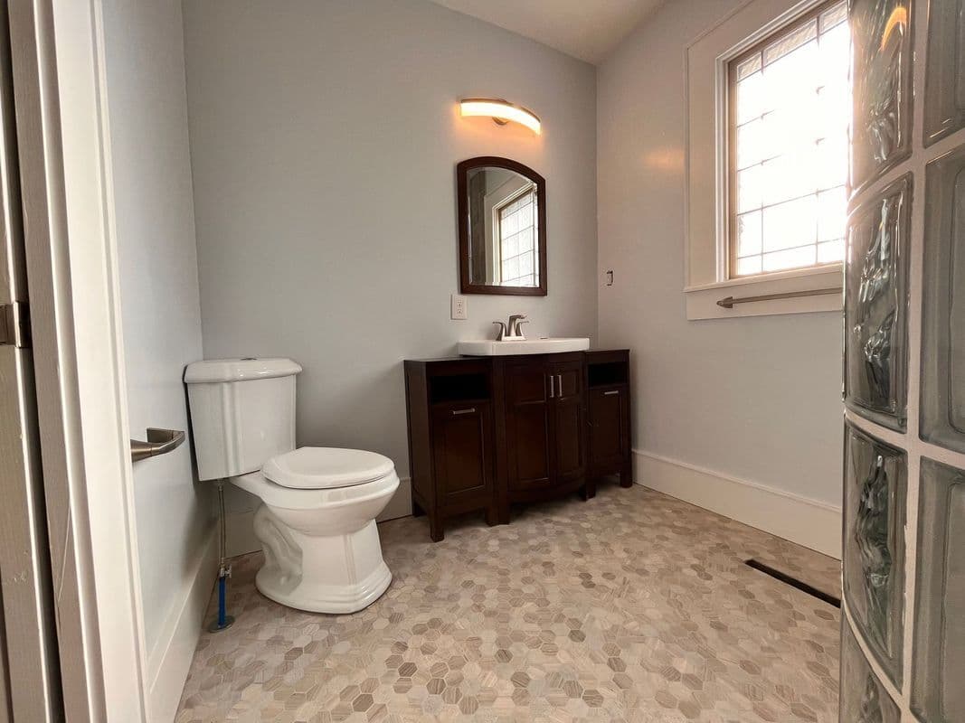 Modern bathroom with white toilet, dark wood vanity, and natural light from a glass block window.