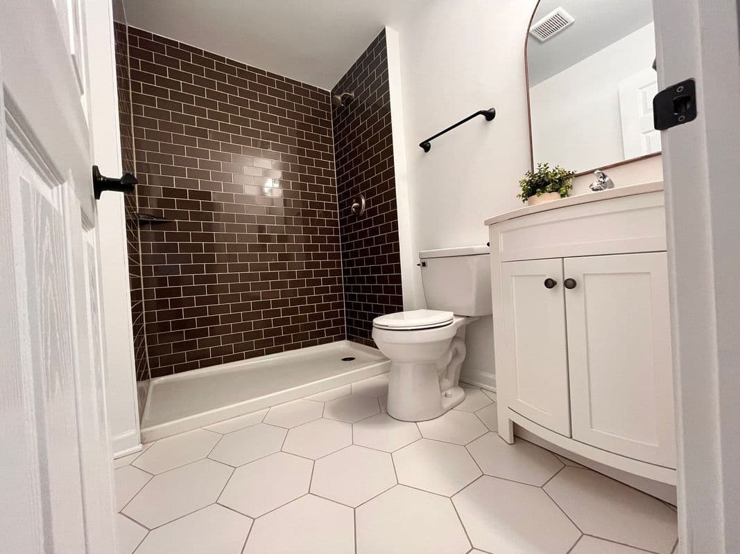 Modern bathroom with brown tiled shower, hexagonal floor tiles, and white vanity storage.