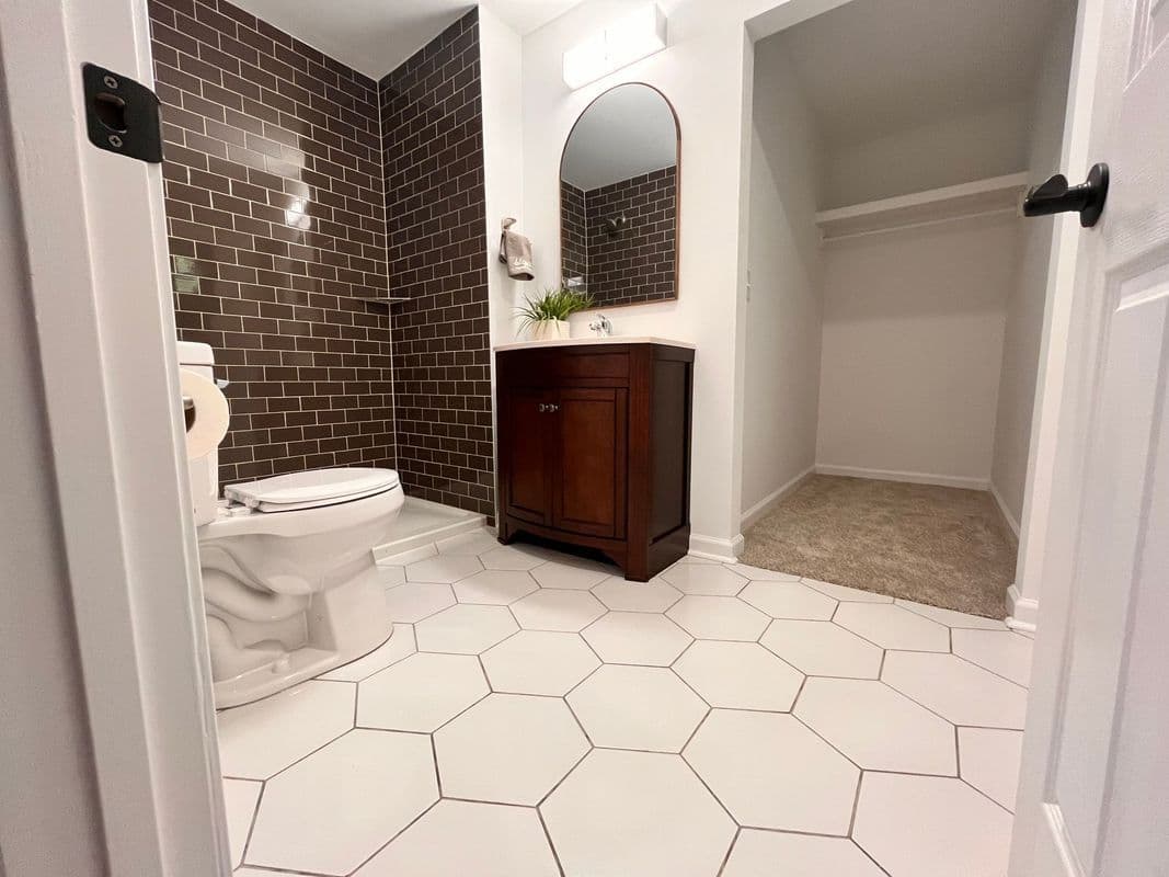 Modern bathroom featuring brown tiled wall, white hexagon floor, wooden vanity, and closet.