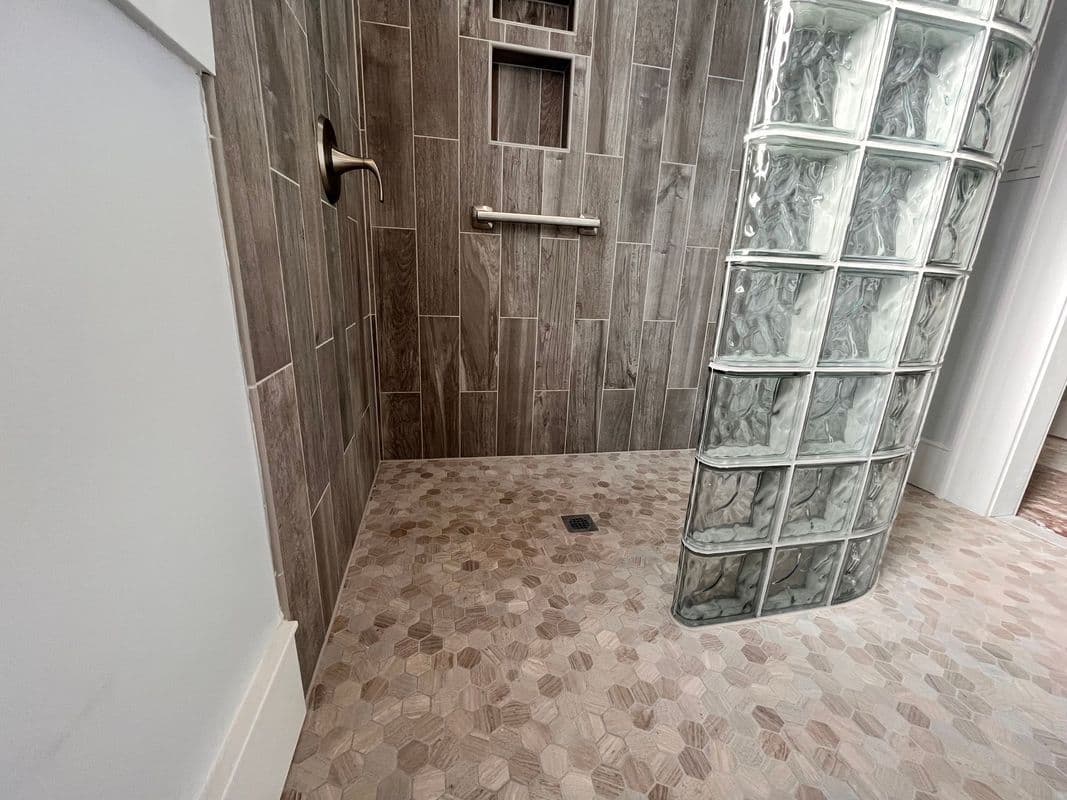 Modern bathroom shower with textured tile wall, glass block feature, and stone floor.