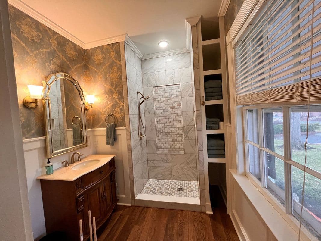 Elegant bathroom design featuring a marble shower, wooden vanity, and ample natural light.