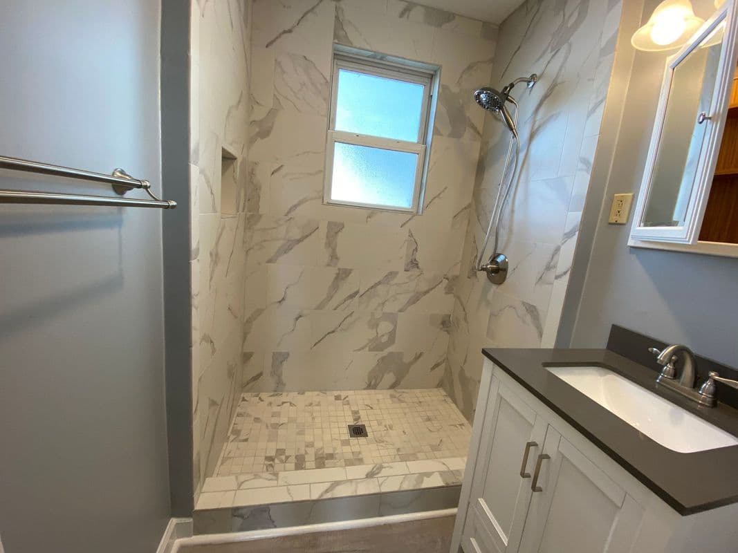 Elegant bathroom shower featuring marble tiles, glass window, and modern fixtures.