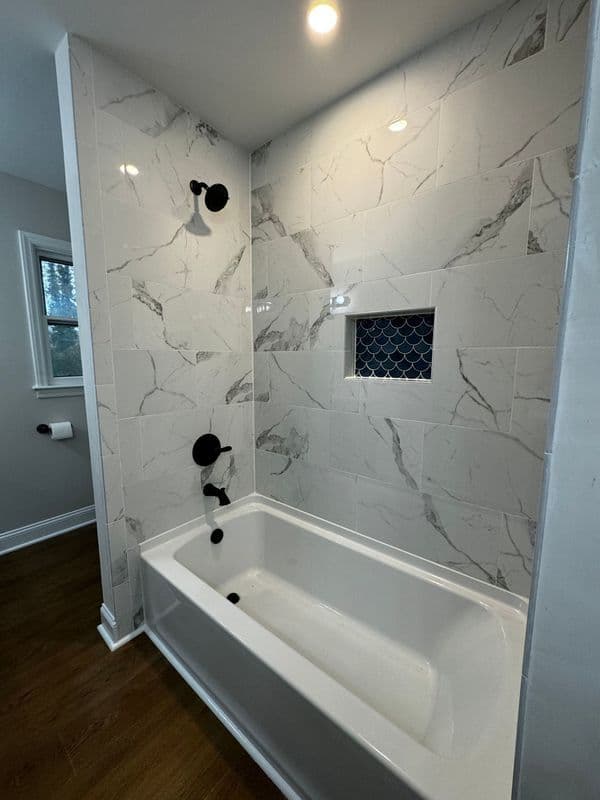Modern bathroom with a marble tile shower, black fixtures, and a built-in niche for toiletries.