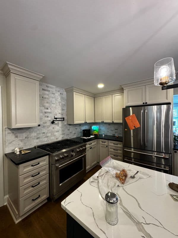 Modern kitchen with stainless steel appliances, marble countertops, and light cabinetry.