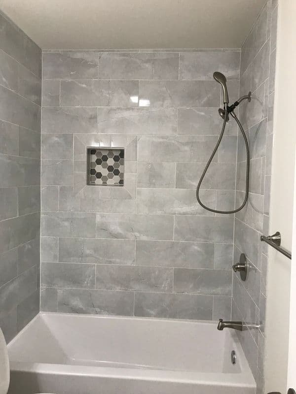 Modern bathroom with gray tiled walls, shower fixture, and built-in alcove for toiletries.