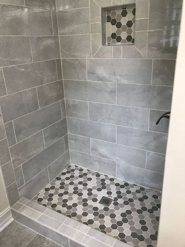 Modern shower design featuring gray tile, hexagonal floor tiles, and built-in niche.