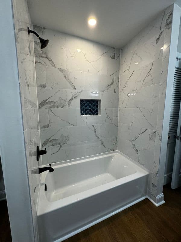 Modern bathroom featuring a white bathtub, elegant marble tiles, and sleek black fixtures.