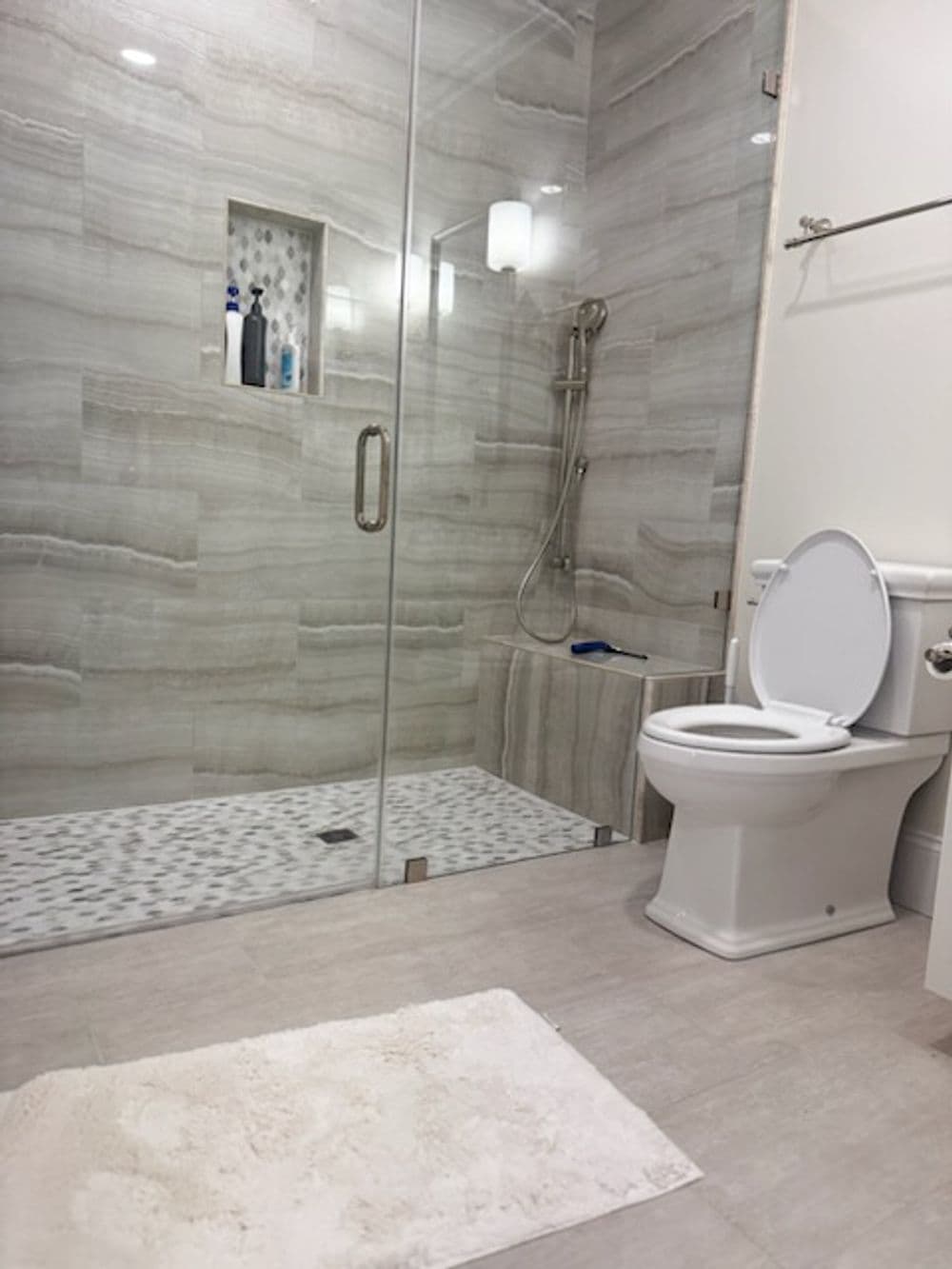 Modern bathroom featuring a glass shower, white toilet, and marble tile flooring.