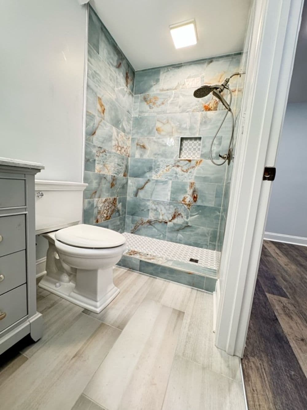 Modern bathroom with blue marble shower, white toilet, and light wood flooring.