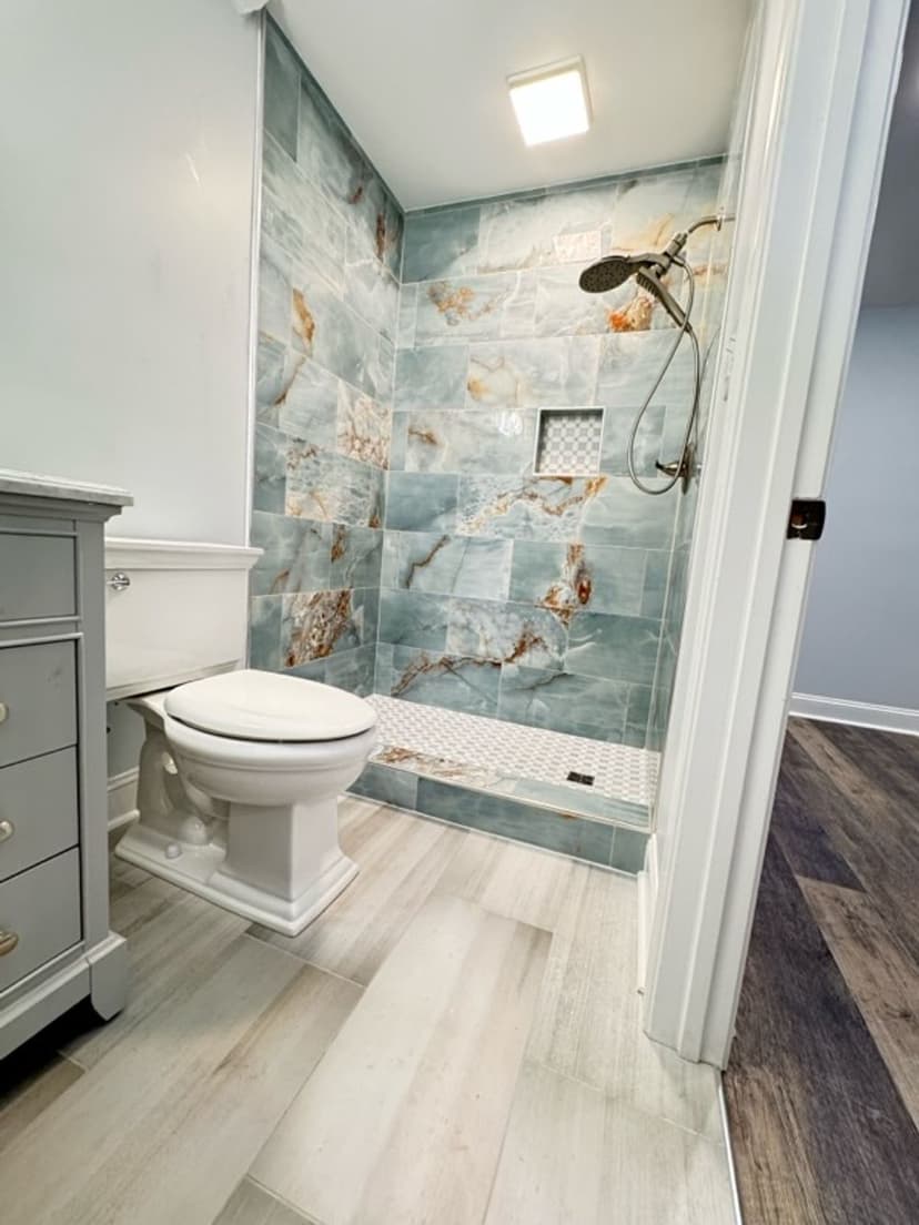 Modern bathroom with blue marble shower, white toilet, and stylish wood flooring.
