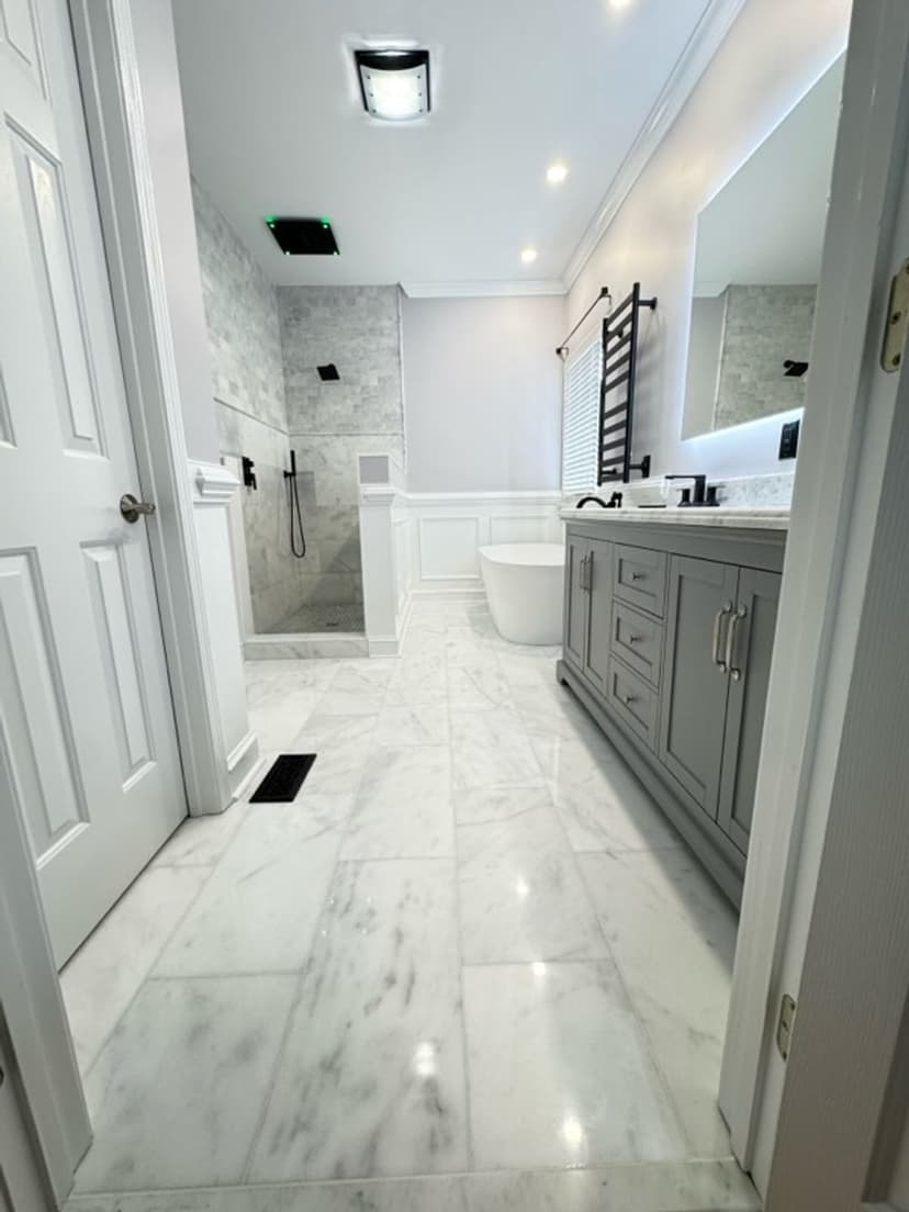 Modern bathroom with marble flooring, gray cabinetry, large mirror, and glass shower enclosure.
